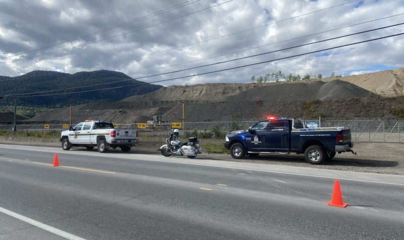 One white DFO truck, one dark blue conservation truck, and one RCMP motorcycle parked on the side of the road.