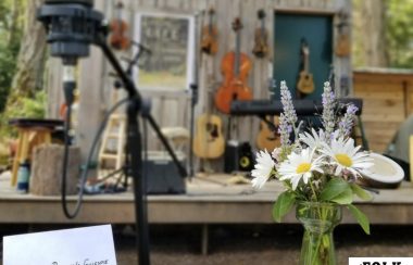 A name card and flower bouquet with microphone in the foreground, string instruments hanging on an outdoor wall in the background.