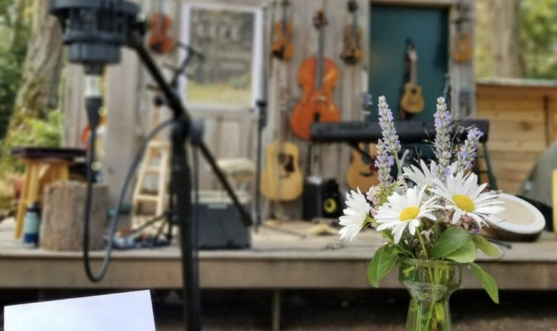 A name card and flower bouquet with microphone in the foreground, string instruments hanging on an outdoor wall in the background.