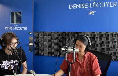 Phi-Vân Nguyen à droite, lors de notre entrevue et derrière se trouve un mur bleu sur lequel est écrit Studio Denise-Lécuyer.