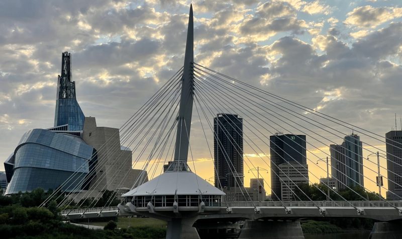Le musée des droits de l'homme et le pont, qui sont des sites très populaires dans la ville de Winnipeg, sont visibles à gauche de la photo, ainsi que le coucher de soleil et les nuages dans le ciel.