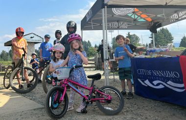 A group of children with bicycles at a station with a tent and a city of Nanaimo banner draped over a table.
