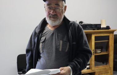 Un homme d'âge mûr portant casque, lunettes et coupe-vent tient une liasse de documents dans ses mains