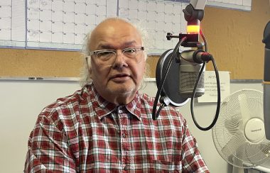 Man sits at Microphone wearing checkered red shirt in CKRZ studio, looking at camera