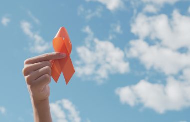 Une main tient un symbole de solidarité orange dans le ciel. Le lied est bleu avec des nuages.