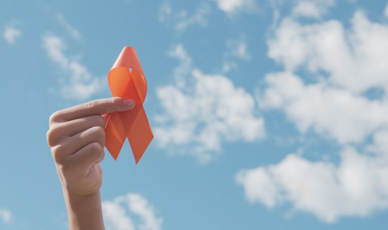 Une main tient un symbole de solidarité orange dans le ciel. Le lied est bleu avec des nuages.