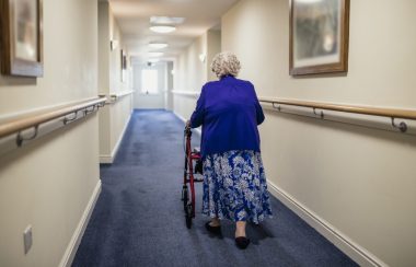 Une femme âgée marchant dans un couloir avec l'aide d'un déambulateur. vue de derrière.