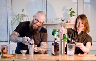 Glenn Barrington and Anne Herteis make cocktails side by side, behind a bar.