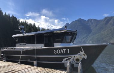 A boat with a large cabin is docked, with mountains in the background.