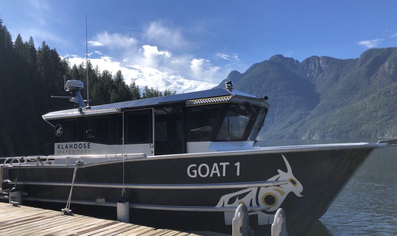 A boat with a large cabin is docked, with mountains in the background.