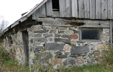 On peut voir une grange ancienne avec un solage en pierre sise et un toit en planches et en tôles.