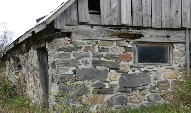 On peut voir une grange ancienne avec un solage en pierre sise et un toit en planches et en tôles.