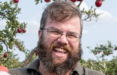 A headshot of Greg Graham standing in front of an apple tree wearing glasses and sporting a beard.