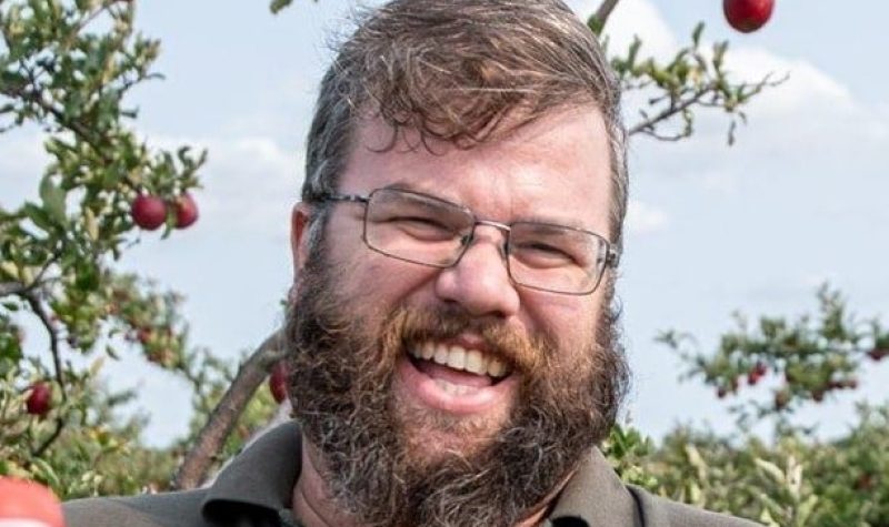 A headshot of Greg Graham standing in front of an apple tree wearing glasses and sporting a beard.