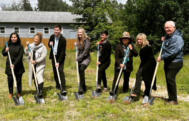 Eight people pose with shovels in the grass at groundbreaking ceremony