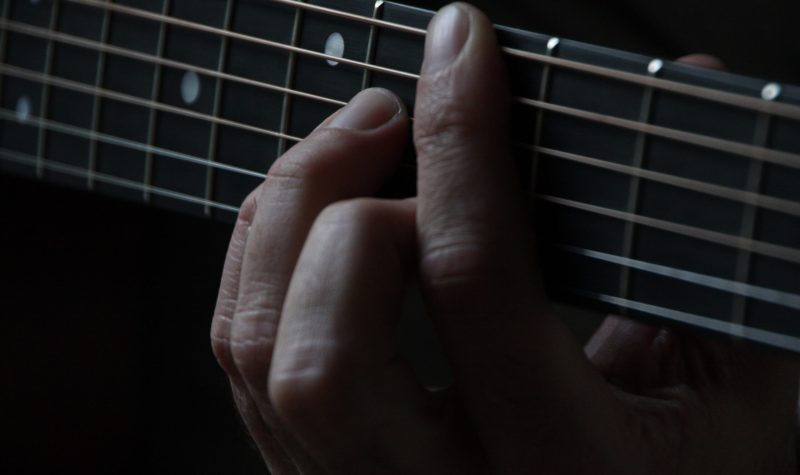 Une main pinçant les cordes d'une guitare