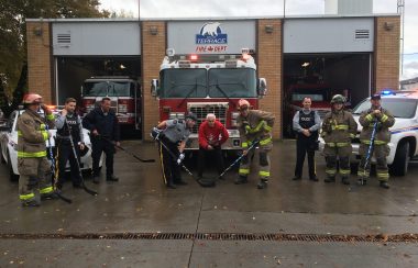 Firefighters and RCMP Officers pose in front of a fire truck in a hockey puck drop stance