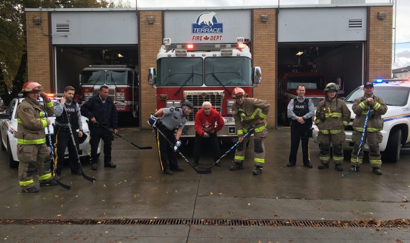 Firefighters and RCMP Officers pose in front of a fire truck in a hockey puck drop stance
