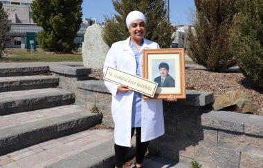 Dr. Kandola stands in front of stone steps with a photo of her father