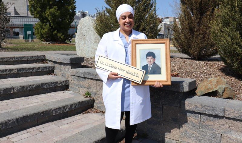 Dr. Kandola stands in front of stone steps with a photo of her father