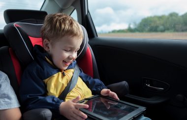Enfant dans son siege auto, il souri en regardant une tablette.