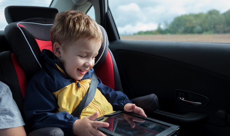 Enfant dans son siege auto, il souri en regardant une tablette.