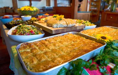 Fresh baking and vegetarian dishes are displayed on a buffet table, adorned with sunflowers.