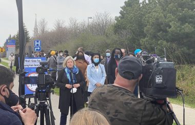 People standing in front of cameras and speaking outside on a sidewalk.