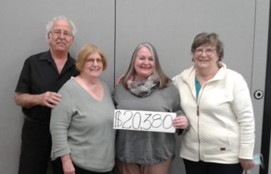 Four people stand together with a sign displaying the $20,300 raised in the 2021 hospital hustle fundraiser