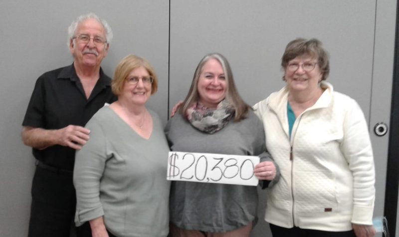 Four people stand together with a sign displaying the $20,300 raised in the 2021 hospital hustle fundraiser