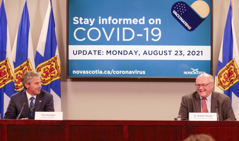 Two men sit behind a desk with Nova Scotia flags behind them