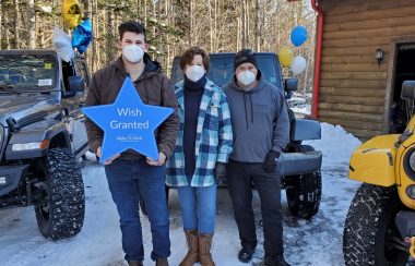 Three people stand in front of a jeep. One holds a blue Make-A-Wish star in his hands.