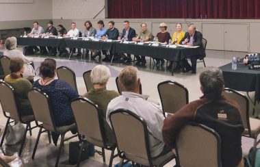 A room full of people sits before 12 people all at a table together.