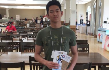 A man standing in a cafeteria holding brochures.