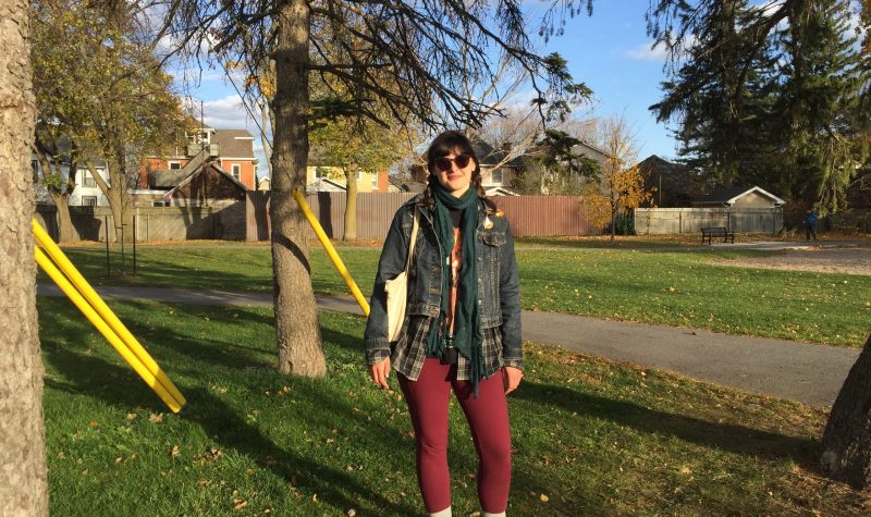 A woman wearing a jacket and sunglasses standing in front of trees