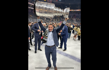A man in a suit lifting the Stanley Cup over his head. People in the background are smiling.
