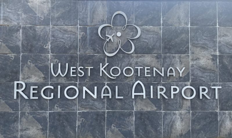 Grey sign that says West Kootenay Regional Airport. Logo above print.