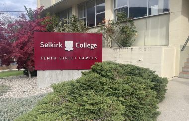 Sign that reads Selkirk COllege tenth street campus. Bush in front, trees behind.
