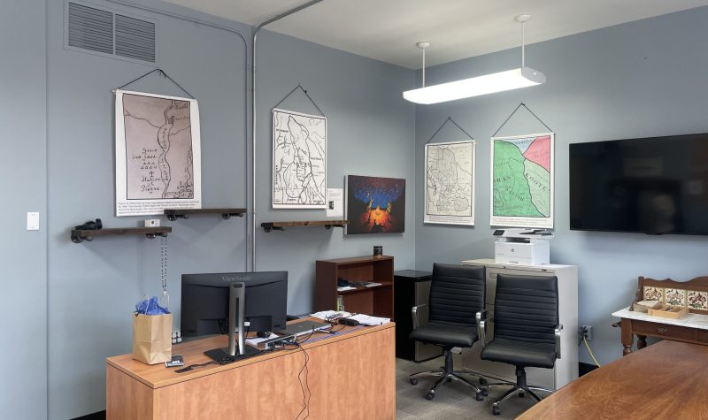 Office with a desk, chairs and maps on the walls.