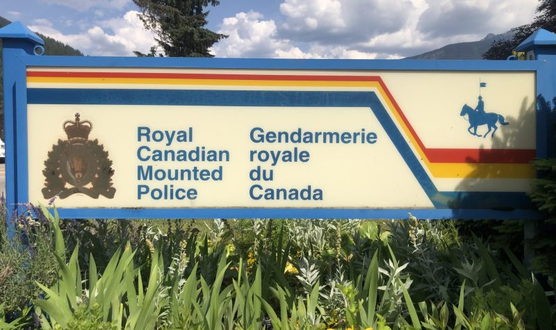 A rectangular sign in with logo of the RCMP in a garden of yellow, orange and blue flowers.