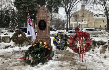 La pierre tombale de Louis Riel est entourée de quatre couronnes de fleurs avec de la neige sur le sol.
