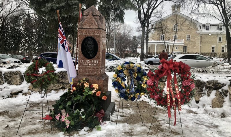 La pierre tombale de Louis Riel est entourée de quatre couronnes de fleurs avec de la neige sur le sol.