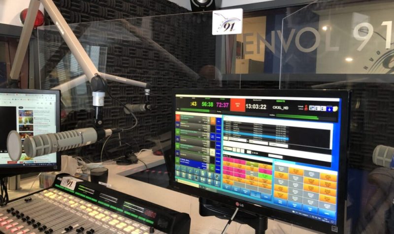 Le studio de la radio, une console allumée est sur le comptoir à gauche avec un écran à la droite qui montre la programmation de l'émission.