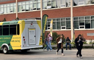 Un bus jaune vert avec des étudiants qui descendent et se dirigent vers l’entrée du bâtiment