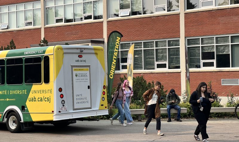 Un bus jaune vert avec des étudiants qui descendent et se dirigent vers l’entrée du bâtiment