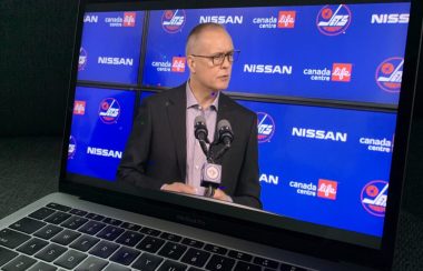 Un ordinateur portable joue la conférence de presse montrant Paul Maurice devant un micro avec un arrière-plan bleu couvert de logos des Jets