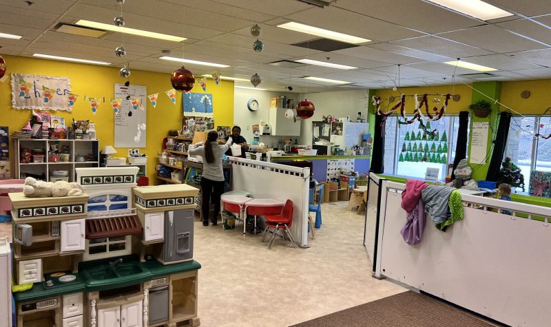 Une salle, décorée avec différents objets pour enfants, avec des tables sur les quelles il y a des livres, des jouets et des nounous deux personne debout en train de discuter