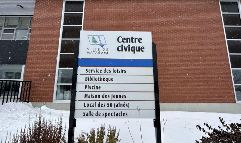 Panneau de présentation du centre civique de Matagami en avant de l'édifice de briques.