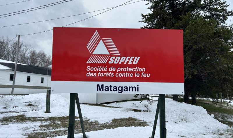 Panneau écriteau rouge et blanc de la société de protection des forêts contre le feu à Matagami. Il y à des plaques de neige au sol dans l'herbe au pied du panneau.