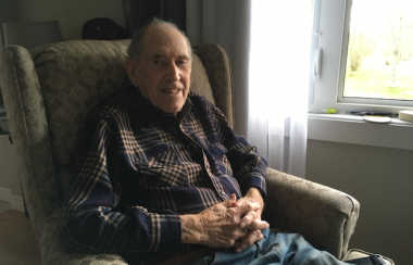 An older man sitting in an armchair beside a window.